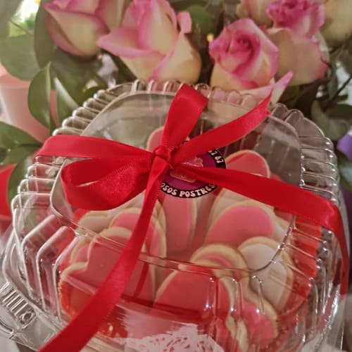 galletas de mantequilla de corazón con glaseado de royal icing con fondo de un ramo de rosas
